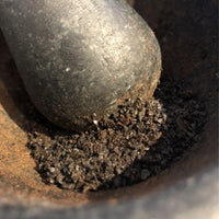Black garlic granules crushed in stone mortar with stone pestle